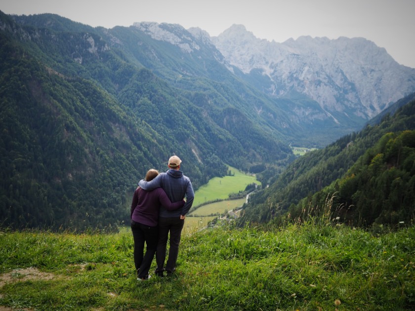 two people looking over green Valley in Slovenia with towering mountains behind